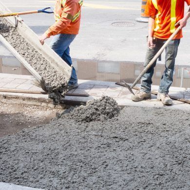 Concreting workers with shovels and hard hats pouring concrete